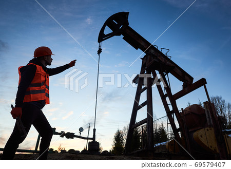 Silhouette of a worker and an oil pump jack on the sunset agains beautiful sky 69579407