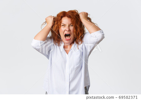Angry and hateful middle-aged redhead woman looking outraged and bothered, grimacing from hatred, furiously ripping hair out of head, screaming bothered and annoyed, white background Angry and hateful middle-aged redhead woman looking outraged and bothered, grimacing from hatred, furiously ripping hair out of head, screaming bothered and annoyed, white background 69582371