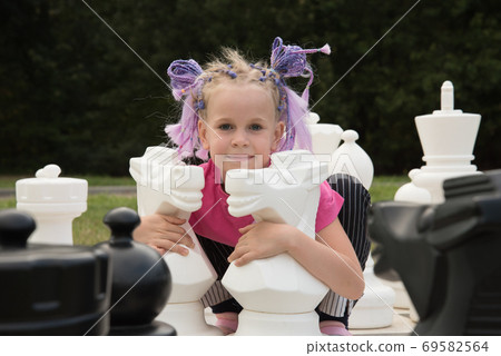 The girl hugs huge chess pieces. Two white horses. The concept of learning a chess game. Grandmaster. The girl hugs huge chess pieces. Two white horses. The concept of learning a chess game. Grandmaster. 69582564