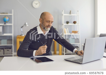 An elderly man works using a laptop office at home. An elderly man works using a laptop office at home. 69587678
