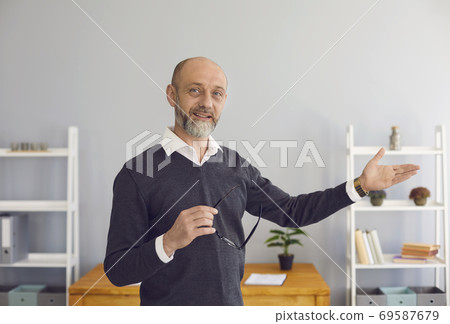A middle-aged male professor looking at the camera uses web chat, says a business strategy remotely in a room at home. A middle-aged male professor looking at the camera uses web chat, says a business strategy remotely in a room at home. 69587679