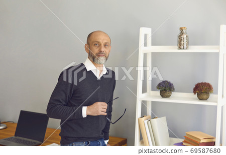A middle-aged teacher professor with glasses in his hands at the workplace. 69587680