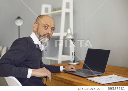Online job concept. Serious elderly man working or studying at home on his laptop computer, mockup for design Online job concept. Serious elderly man working or studying at home on his laptop computer, mockup for design 69587681