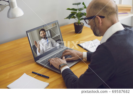 A male patient writes a message to a doctor. An online video chat uses a laptop. A male patient writes a message to a doctor. An online video chat uses a laptop. 69587682