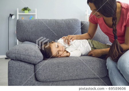 Happy young mother watching her daughter sleep on sofa in living room. Parent admiring her napping kid at home Happy young mother watching her daughter sleep on sofa in living room. Parent admiring her napping kid at home 69589606