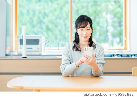 Middle-aged woman operating a smartphone in the dining room Middle-aged woman operating a smartphone in the dining room 69592652