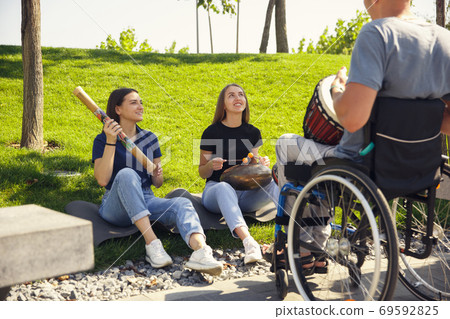 Happy handicapped man on a wheelchair spending time with friends playing live instrumental music outdoors Happy handicapped man on a wheelchair spending time with friends playing live instrumental music outdoors 69592825