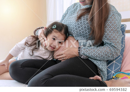 Pregnant young mother sitting on the bed with her little cute daughter 69594382
