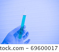 A scientist's hand in a glove holding a glass test tube with a blue liquid inside, color tones. close-up 69600017