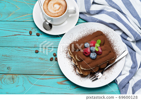 portion of Classic tiramisu dessert with raspberries and blueberries and cup of espresso coffee on blue wooden background portion of Classic tiramisu dessert with raspberries and blueberries and cup of espresso coffee on blue wooden background 69600128