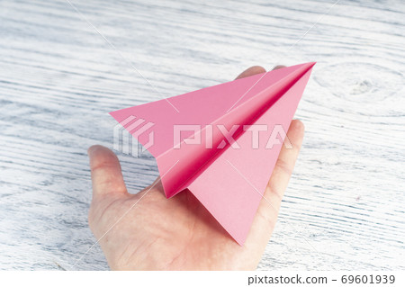 Hand of a teenager holds a pink plane on a white wooden background. 69601939
