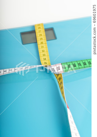 Aquamarine floor scales wrapped in a multicolored centimeter on a white background. Tied in a knot. Tools for controlling weight and body parameters when dieting Aquamarine floor scales wrapped in a multicolored centimeter on a white background. Tied in a knot. Tools for controlling weight and body parameters when dieting 69601975