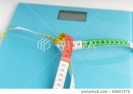 Aquamarine floor scales wrapped in a multicolored centimeter. Tied in a knot. Tools for measuring weight and body parameters when dieting Aquamarine floor scales wrapped in a multicolored centimeter. Tied in a knot. Tools for measuring weight and body parameters when dieting 69601978