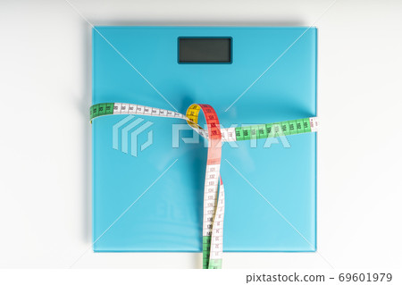 Aquamarine floor scales wrapped in a multicolored centimeter on a white background. Tied in a knot. Tools for measuring weight and body parameters when dieting 69601979