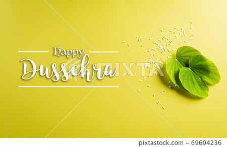 Happy Dussehra background concept. Green leaf and rice on yellow pastel background. Dussehra Indian Festival concept. 69604236