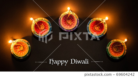 Happy Diwali - Clay Diya lamps lit during Dipavali, Hindu festival of lights celebration. Colorful traditional oil lamp diya on black background Happy Diwali - Clay Diya lamps lit during Dipavali, Hindu festival of lights celebration. Colorful traditional oil lamp diya on black background 69604242
