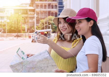 Traveler two young woman holding map in hand together while pointing direction. 69605332