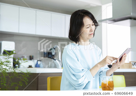 A middle-aged woman looking at a smartphone in the kitchen A middle-aged woman looking at a smartphone in the kitchen 69606649
