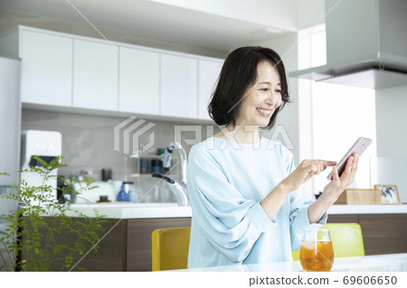 A middle-aged woman looking at a smartphone in the kitchen A middle-aged woman looking at a smartphone in the kitchen 69606650