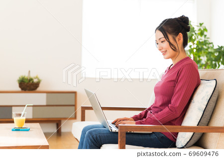 坐沙發和操作計算機的婦女 坐沙發和操作計算機的婦女 69609476