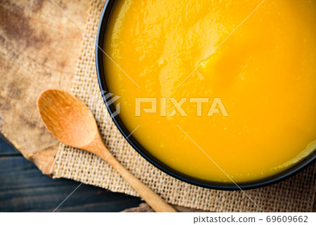 Close up of pumpkin soup in a bowl with spoon on wooden background 69609662