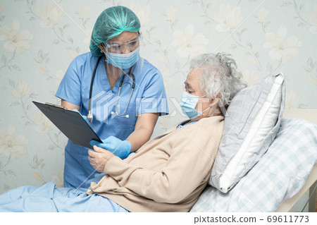 Asian doctor wearing face shield and PPE suit new normal with patient protect Covid-19 Coronavirus. 69611773
