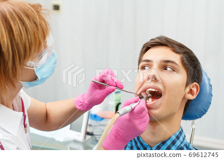 Female dentist is treating a patient tooth in dental office with focus on patient mouth 69612745