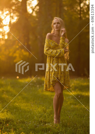 Blond woman resting in forest at sunset Blond woman resting in forest at sunset 69613394