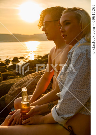 Couple relaxing and drinking beer at the beach at sunset 69615263
