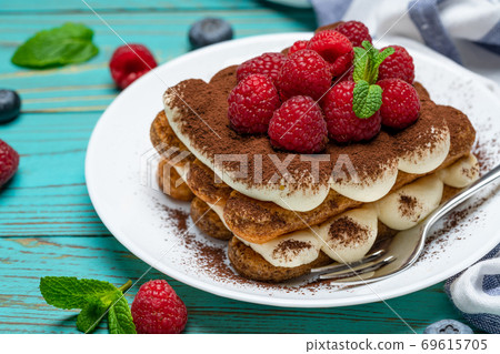 portion of Classic tiramisu dessert with raspberries and blueberries on blue wooden background 69615705