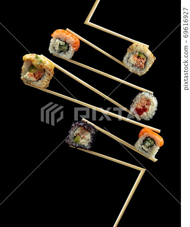 Fresh tasty sushi in wooden chopsticks on a black background. 69616927
