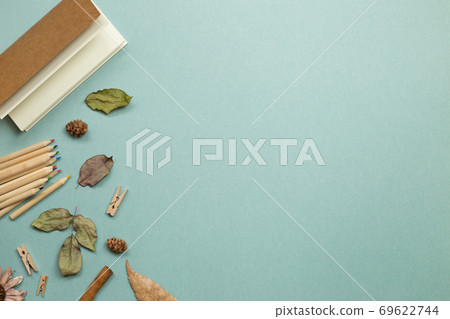 Autumn concept. Notebook and wooden colored pencils with dry leaves on green background. flat lay, top view, copy space. Work and study place 69622744