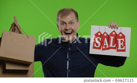 Surprised guy showing shopping bags and Sale word, looking astonished by low cost purchase, discount Surprised guy showing shopping bags and Sale word, looking astonished by low cost purchase, discount 69627115