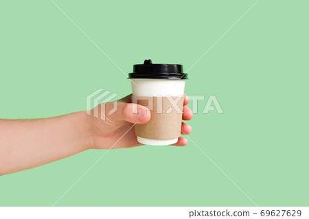 Mockup of male hand holding a White paper kraft disposable cup for coffee with black plastic lid on light green background. Take-away cup. Space for text, copy space. Mockup of male hand holding a White paper kraft disposable cup for coffee with black plastic lid on light green background. Take-away cup. Space for text, copy space. 69627629