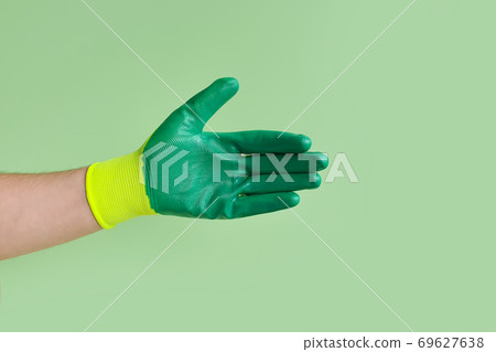 Male hand in a glove for working in the garden, vegetable garden on a green background. Open hand for handshake. Male hand in a glove for working in the garden, vegetable garden on a green background. Open hand for handshake. 69627638