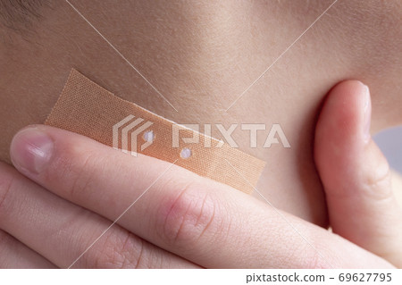 Adhesive plaster on the neck of a teenager on a wound. Hand touches a sore spot. Adhesive plaster on the neck of a teenager on a wound. Hand touches a sore spot. 69627795