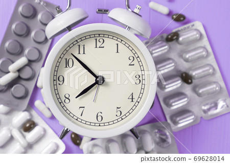 Alarm clock in a heap blister packs with medical pills on a bright neon purple background. Idea of sleep control Alarm clock in a heap blister packs with medical pills on a bright neon purple background. Idea of sleep control 69628014