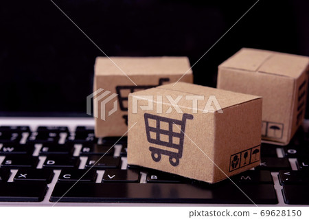 Shopping online. Cardboard box with a shopping cart logo on laptop keyboard. Shopping service on The online web. offers home delivery. Shopping online. Cardboard box with a shopping cart logo on laptop keyboard. Shopping service on The online web. offers home delivery. 69628150