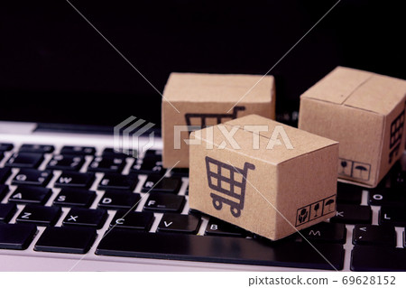 Shopping online. Cardboard box with a shopping cart logo on laptop keyboard. Shopping service on The online web. offers home delivery. Shopping online. Cardboard box with a shopping cart logo on laptop keyboard. Shopping service on The online web. offers home delivery. 69628152
