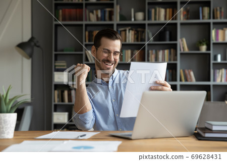 Overjoyed male triumph reading good news in letter 69628431