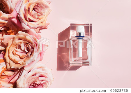Perfume glass bottle with trendy shadow and pink golden roses on a pastel pink background. Bottle for branding and label. Luxurious flatlay. Perfume glass bottle with trendy shadow and pink golden roses on a pastel pink background. Bottle for branding and label. Luxurious flatlay. 69628786