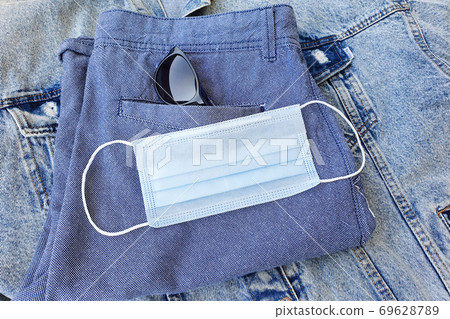 Medical protective face mask on folded blue shorts. Accessories in the modern world. Biological concept of life in a new reality. Top view, flatlay lifestyle. Medical protective face mask on folded blue shorts. Accessories in the modern world. Biological concept of life in a new reality. Top view, flatlay lifestyle. 69628789