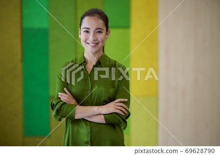 Portrait of a young beautiful female office worker keeping arms crossed, looking at camera and smiling while standing in the modern coworking space 69628790