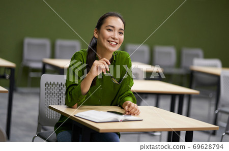 Business training. Young happy woman, female office worker sitting at desk in the office and smiling, listening to coach during corporate seminar Business training. Young happy woman, female office worker sitting at desk in the office and smiling, listening to coach during corporate seminar 69628794