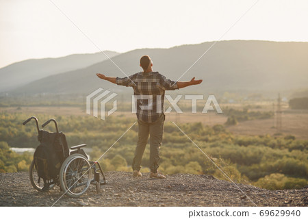 A young man got up to his legs from a wheelchair on top of a mountain at sunrise. The invalid was healed. 69629940