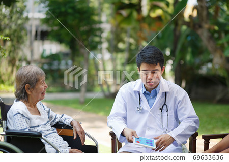 Asian doctor talking with elderly female patient on wheelchair Asian doctor talking with elderly female patient on wheelchair 69633636