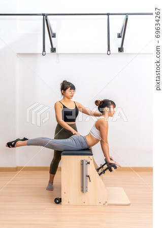 Young Asian woman working on pilates wanda chair machine with her trainer during her health exercise Young Asian woman working on pilates wanda chair machine with her trainer during her health exercise 69634267