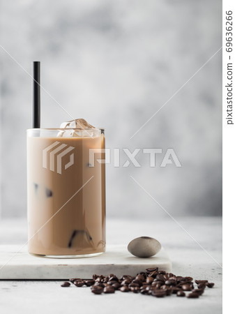 Glass of iced coffee with milk on marble board with spoon and beans on light background 69636266
