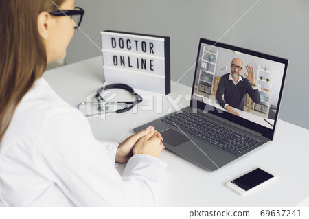 Woman doctor sitting in medical office and looking and greeting her man patient online from laptop Woman doctor sitting in medical office and looking and greeting her man patient online from laptop 69637241