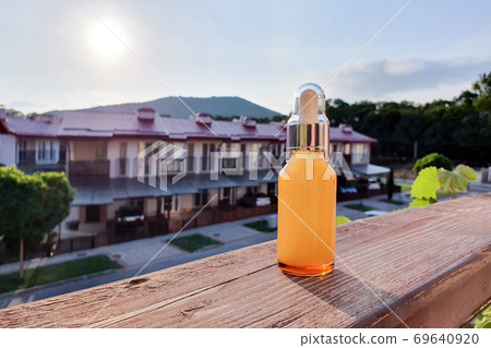 Glass cosmetic bottle with dropper pipette against the sunset. Beauty product for facial skin care, bottle for branding of medicine or cosmetics. Natural organic spa cosmetics concept. Selective Glass cosmetic bottle with dropper pipette against the sunset. Beauty product for facial skin care, bottle for branding of medicine or cosmetics. Natural organic spa cosmetics concept. Selective 69640920